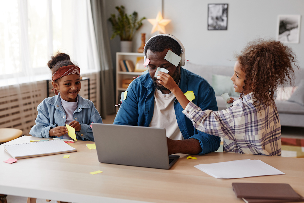 Portrait of two children playing with father trying to work from home, copy space